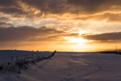 Scenic view of snow covered land against sky during sunset