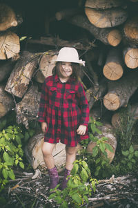 Full length portrait of woman standing by logs in forest