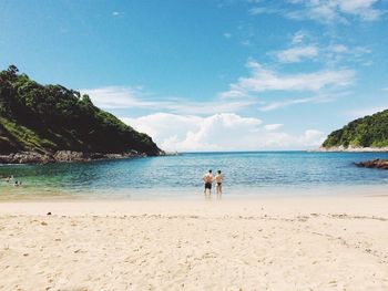 Rear view of man and woman standing on beach against blue sky