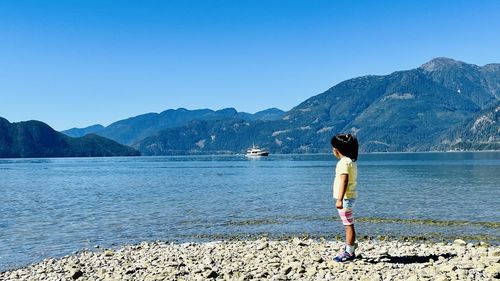 Little  girl standing at lake against mountain