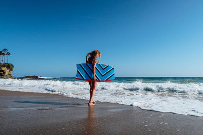 Woman standing on beach against clear blue sky