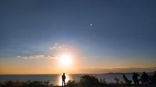 Rear view of woman standing on beach against sky during sunset