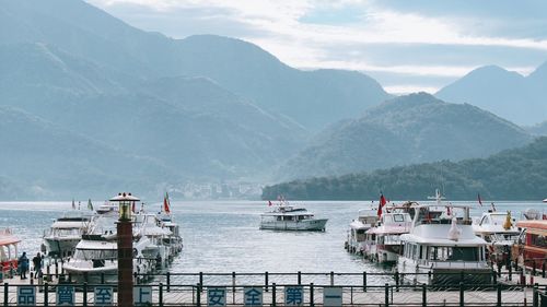 Boats moored at harbor by mountains against sky