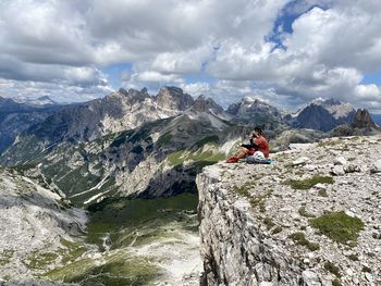 Man on rocks by mountains against sky