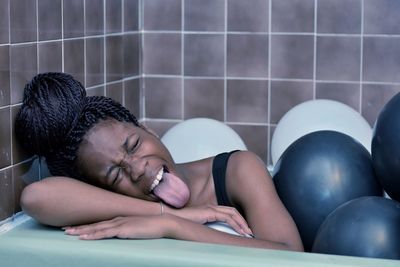 Woman sticking tongue out in tub filled with balloons