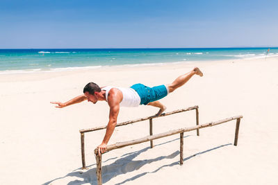 Full length of man exercising at beach against clear sky