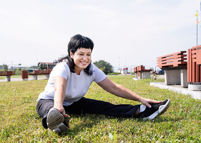 Portrait of smiling young woman sitting on field against sky