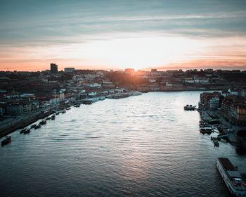 Scenic view of river by buildings against sky during sunset