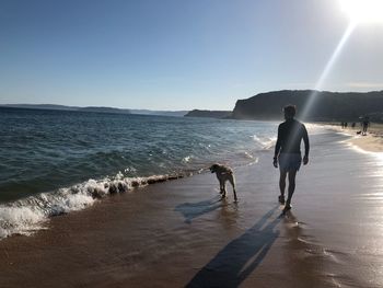 Rear view of men walking on beach against sky