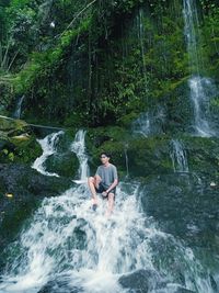 Young man sitting outdoors on waterfall