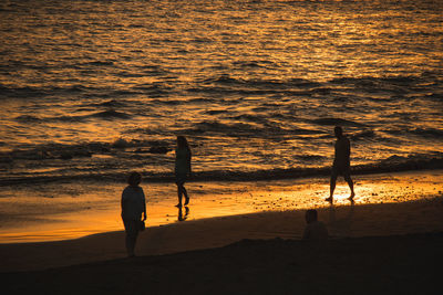 Silhouette people standing on beach during sunset