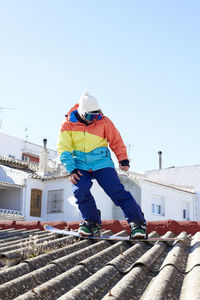 Boy looking at the ground and snowboarding on a roof