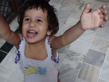 High angle view of cheerful girl looking up while standing with arms raised at home