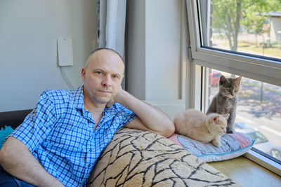 Portrait of a mature man and two cute fluffy kittens on a sofa by the sunny window 