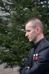 Side view of young man looking away against trees