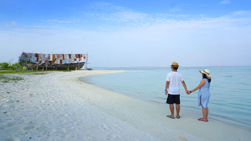 Rear view of people standing on beach against sky