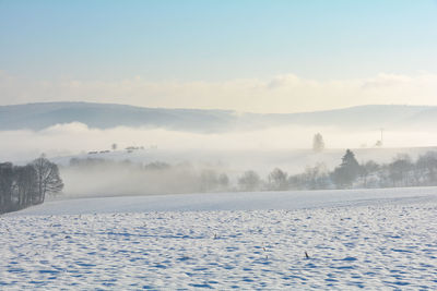 Snow landscape with fields and fog in the valley and with blue sky in spessart, bavaria, germany