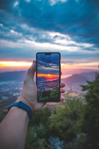 Hand holding mobile phone against sunset sky