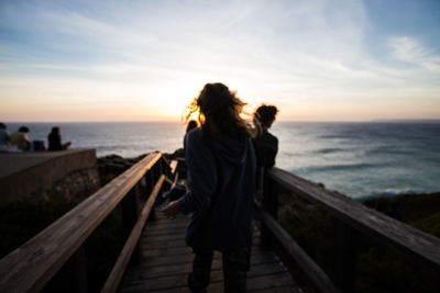 Rear view of woman standing on railing against sea