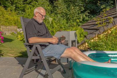Portrait of senior man sitting on chair and putting feet in a pool