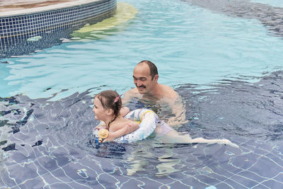 Happy cute asian little girl and her grandfather spend time together in open air thermal pool.