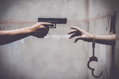 Cropped hand holding gun by person with handcuff
