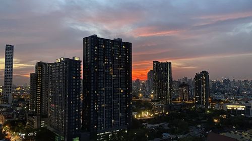 Illuminated buildings in city against sky at sunset