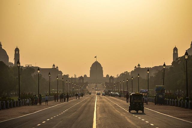 sunset, architecture, built structure, building exterior, clear sky, transportation, copy space, road, the way forward, city, street, car, street light, road marking, silhouette, orange color, diminishing perspective, outdoors, sky, land vehicle