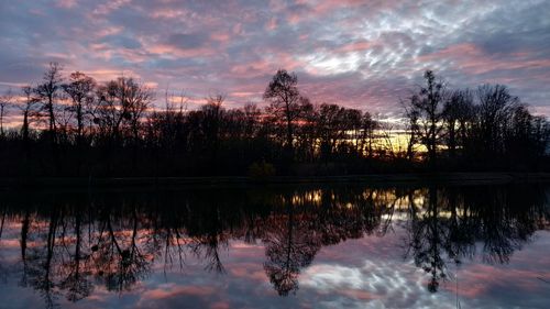 Reflection of silhouette trees in lake against sky during sunset