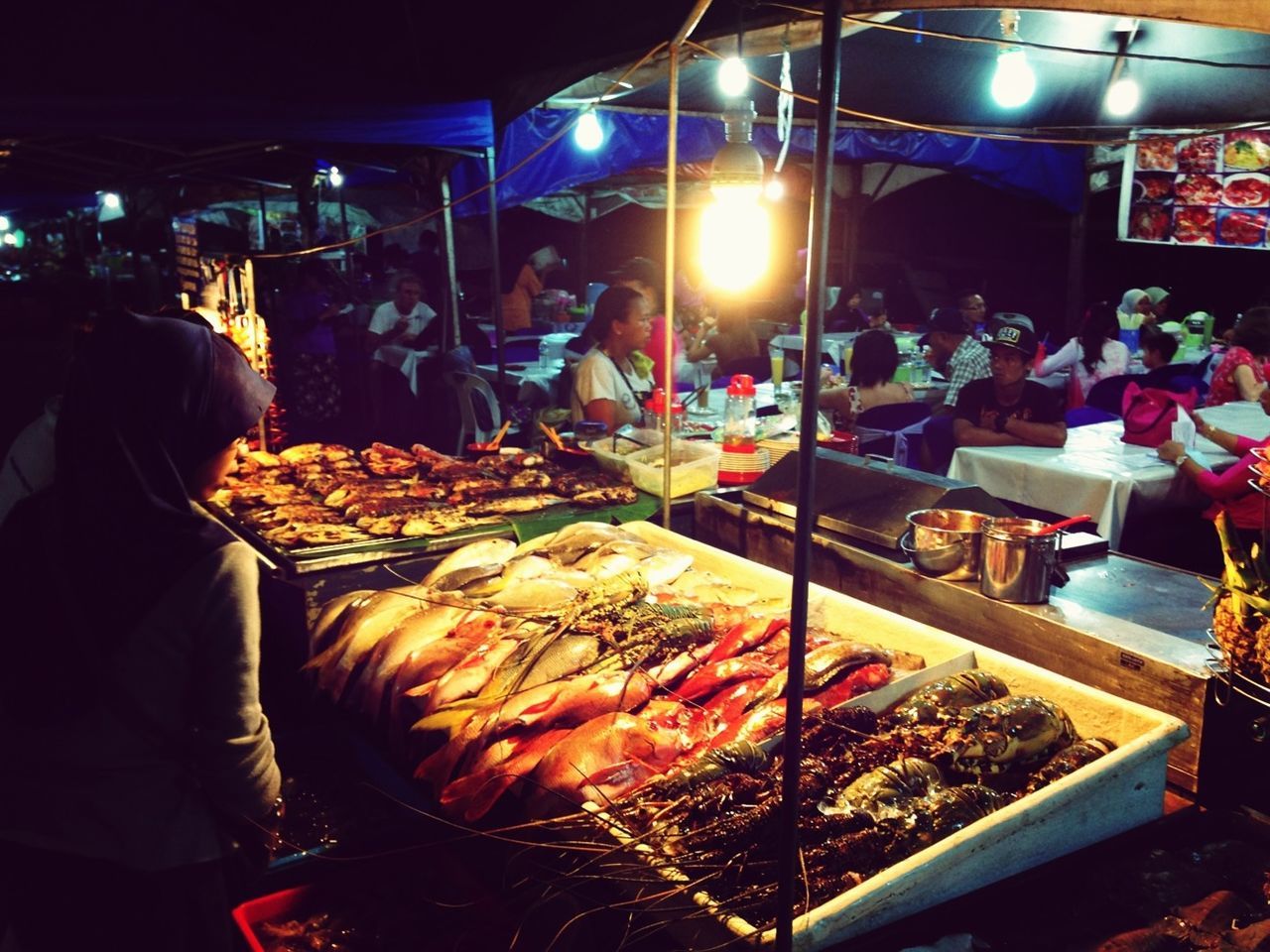 illuminated, night, men, market, retail, food and drink, market stall, food, indoors, lifestyles, for sale, store, incidental people, lighting equipment, person, leisure activity, small business, celebration