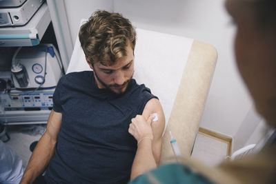 Cropped image of female nurse injecting male patient at hospital