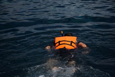 Rear view of man wearing life jacket while swimming in sea