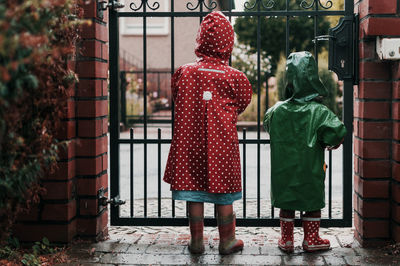 Rear view of children wearing raincoat while standing against gate
