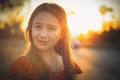 Close-up portrait of smiling teenager girl with long hair on road during sunset
