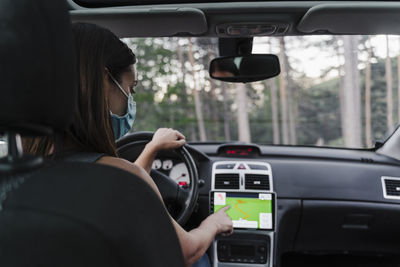 Woman wearing face mask using gps while driving car