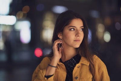 Close-up of young woman looking away while standing outdoors at night