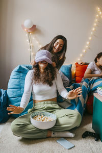 Playful young woman covering eyes of friend at home