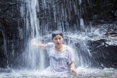 Portrait of smiling woman standing against waterfall