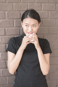 Young woman drinking coffee while standing against wall
