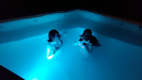 High angle view of women swimming in illuminated pool at night