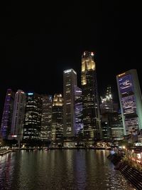 Illuminated buildings by river against sky at night