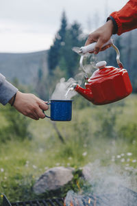 Pouring hot water from a red kettle into a coffee cup in the wilderness while camping