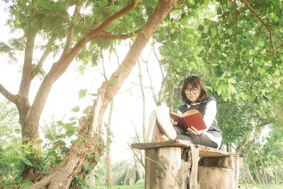 Mature woman reading book while sitting on bench by trees