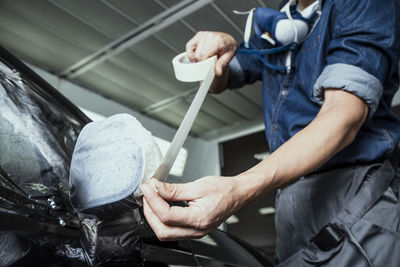 Midsection of mechanic covering car with adhesive tape