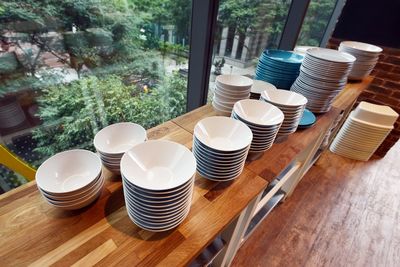 High angle view of stacked bowls and plates on table by glass window