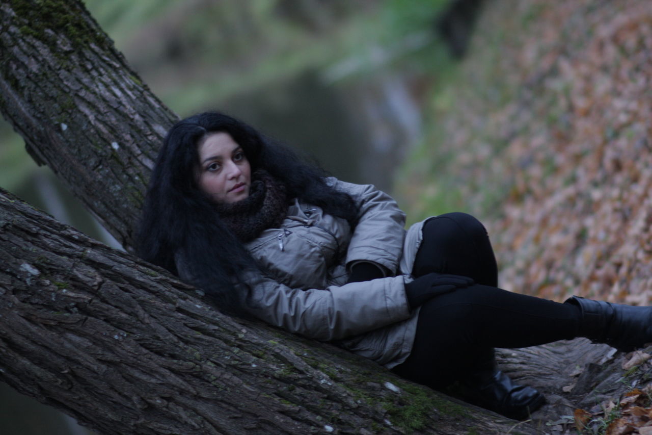 young adult, sitting, lifestyles, young women, leisure activity, casual clothing, warm clothing, full length, tree trunk, person, relaxation, field, focus on foreground, resting, mature adult, outdoors, footpath