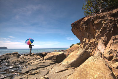 Rear view of woman standing on rock by sea against sky