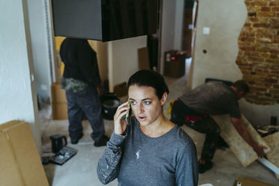 Female construction manager talking on mobile phone at site while workers working in background