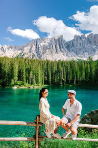 Woman sitting by lake against mountains