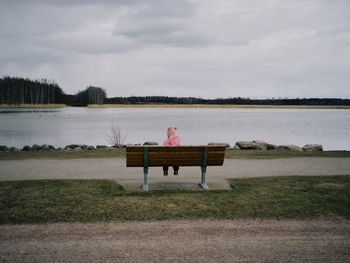 Man sitting on bench by lake against sky